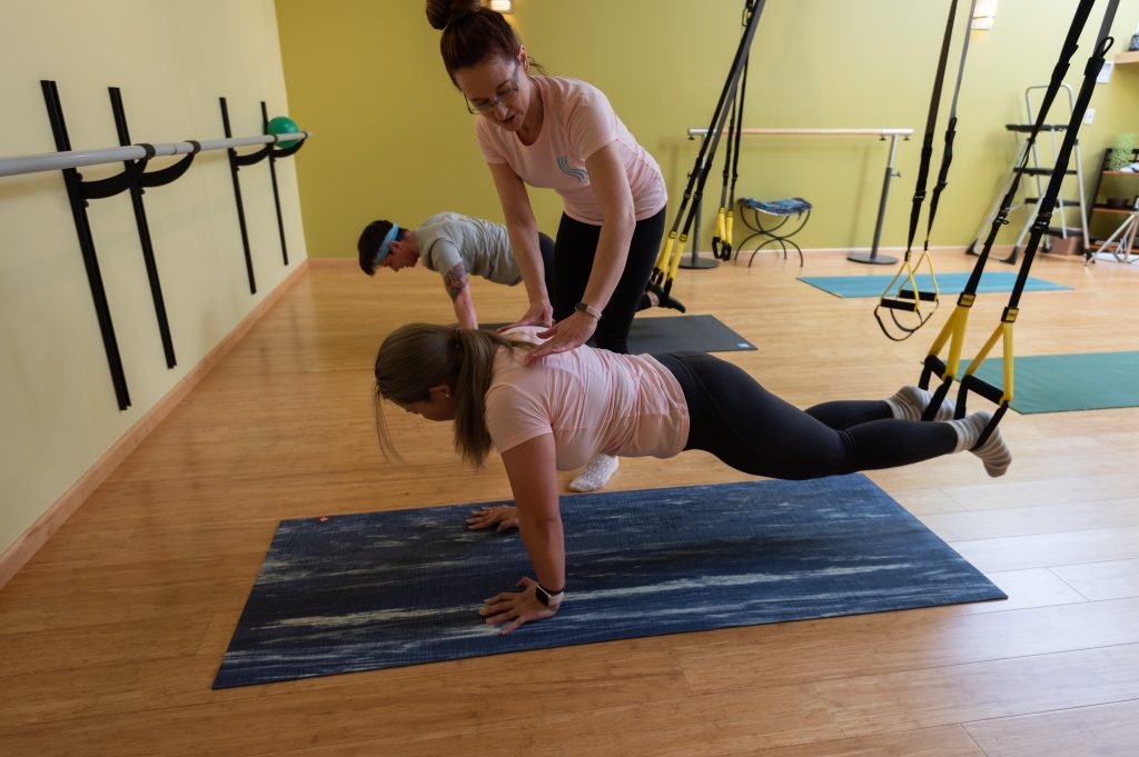 Marcie Evans adjusting a student's suspended plank in a TRX class at Serenity in Iowa City